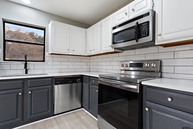 kitchen featuring appliances with stainless steel finishes, light wood-type flooring, decorative backsplash, sink, and white cabinetry