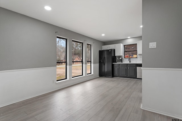 kitchen featuring gray cabinetry, black fridge with ice dispenser, white cabinets, stainless steel dishwasher, and light wood-type flooring