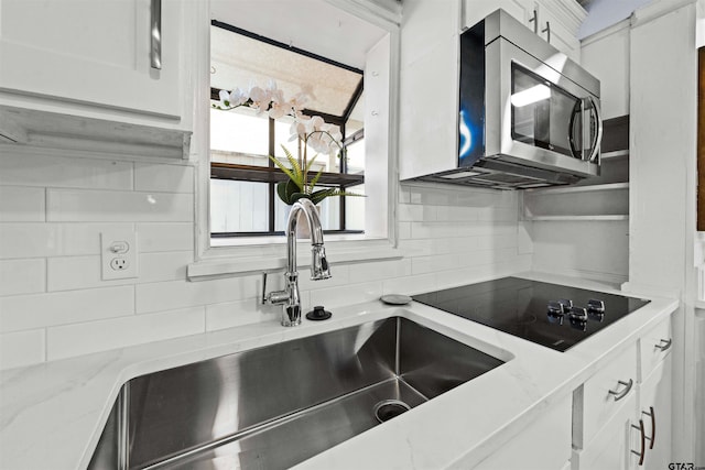 kitchen featuring tasteful backsplash, light stone counters, black electric stovetop, white cabinetry, and sink