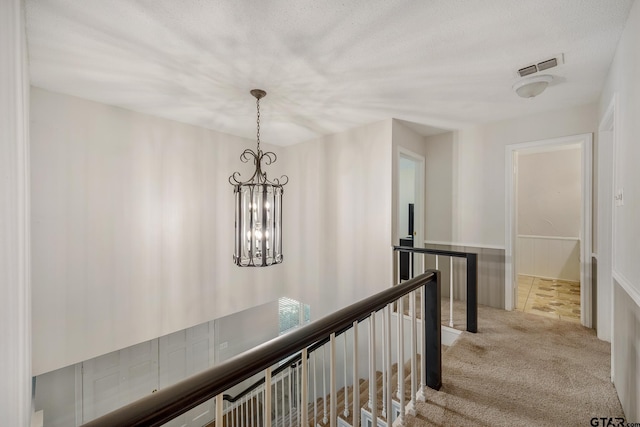 hallway featuring a notable chandelier, visible vents, an upstairs landing, and carpet