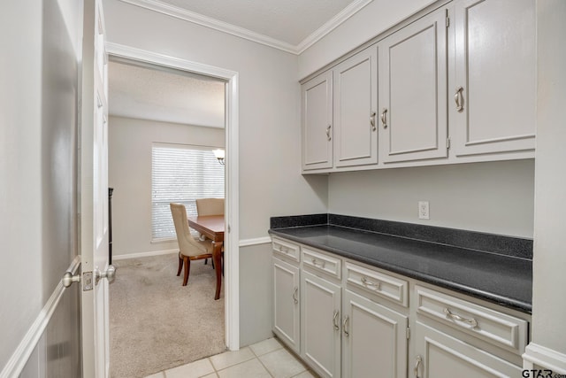 kitchen with light colored carpet, ornamental molding, a textured ceiling, light tile patterned flooring, and dark countertops