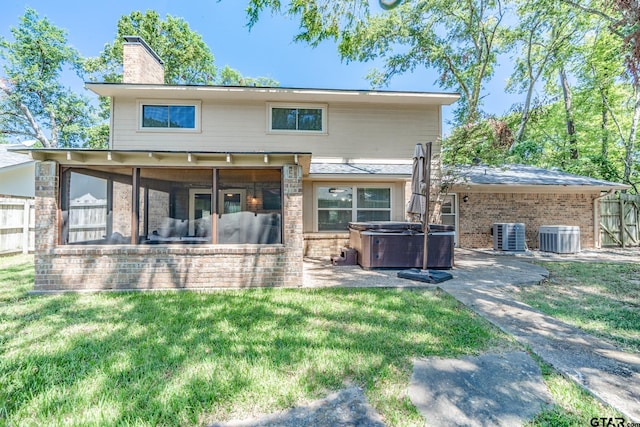 rear view of house featuring a sunroom, fence, a chimney, a lawn, and a hot tub