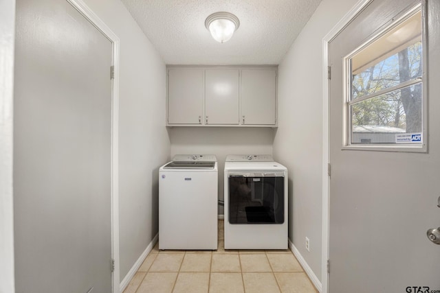 laundry area with a textured ceiling, baseboards, washer and clothes dryer, cabinet space, and light tile patterned floors