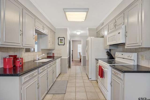 kitchen featuring white appliances, ornamental molding, a sink, dark countertops, and light tile patterned flooring