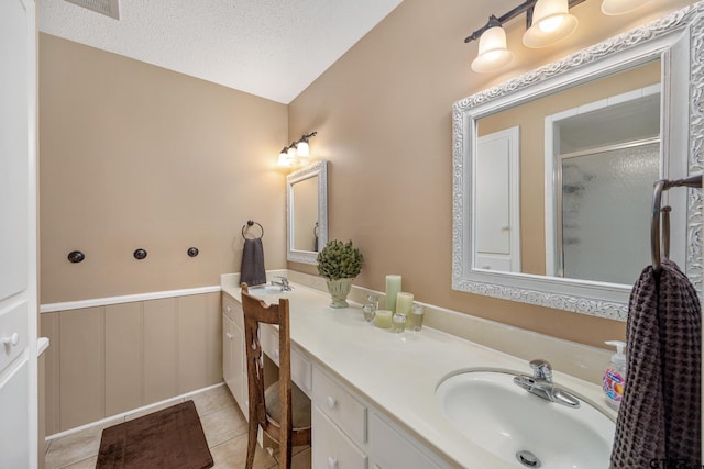 full bath featuring a textured ceiling, a sink, a stall shower, double vanity, and wainscoting