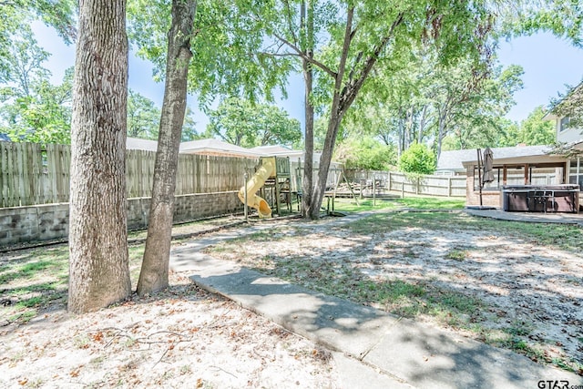 view of yard featuring a hot tub, a fenced backyard, and a playground