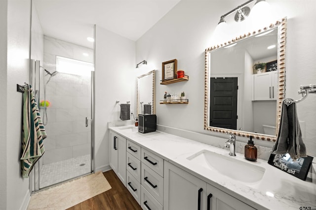 full bathroom with double vanity, a stall shower, a sink, and wood finished floors