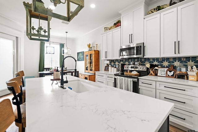 kitchen with a kitchen island with sink, a sink, appliances with stainless steel finishes, decorative backsplash, and crown molding