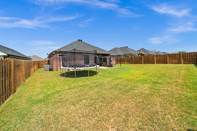 view of yard featuring a trampoline, a fenced backyard, and central AC unit