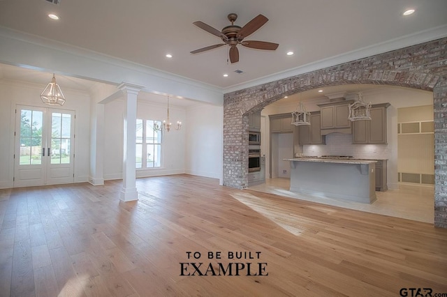 unfurnished living room with french doors, ceiling fan with notable chandelier, crown molding, ornate columns, and light wood-type flooring