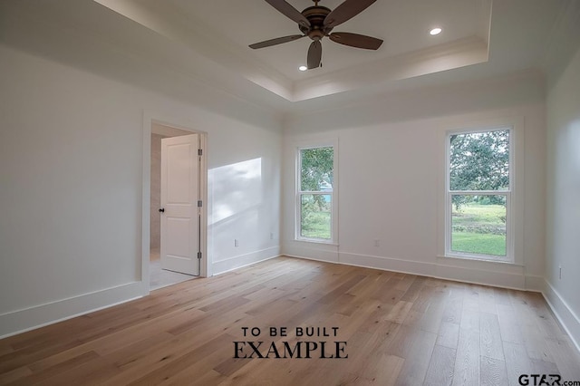 empty room with a raised ceiling, ceiling fan, and light wood-type flooring