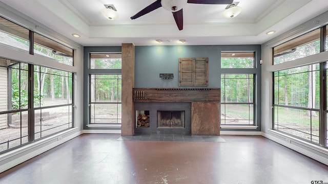 unfurnished living room with plenty of natural light, ceiling fan, a raised ceiling, and a fireplace