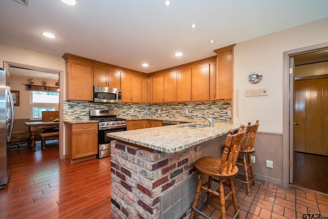 kitchen with stainless steel appliances, sink, kitchen peninsula, light stone counters, and dark wood-type flooring