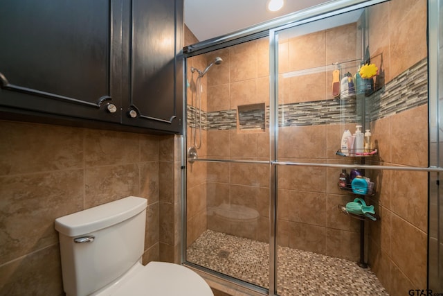 bathroom with a shower with door, toilet, and tile walls