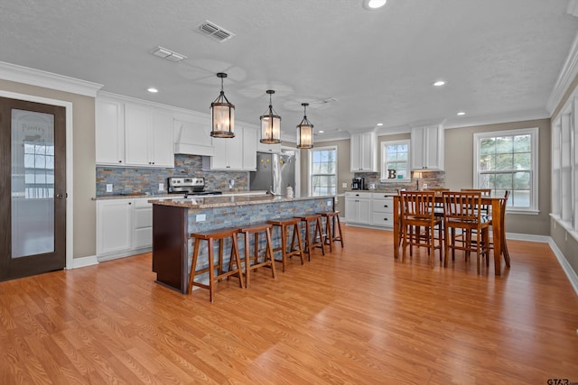 kitchen featuring hanging light fixtures, appliances with stainless steel finishes, white cabinetry, and a kitchen island with sink