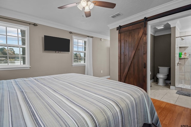 bedroom featuring ensuite bath, ceiling fan, a barn door, light hardwood / wood-style flooring, and ornamental molding