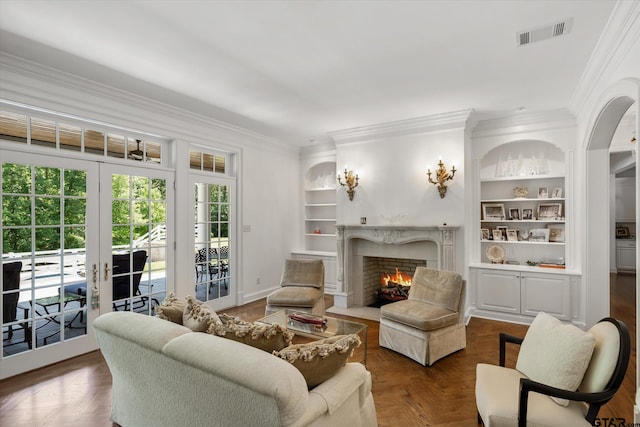 living room with built in features, french doors, ornamental molding, a premium fireplace, and dark parquet flooring