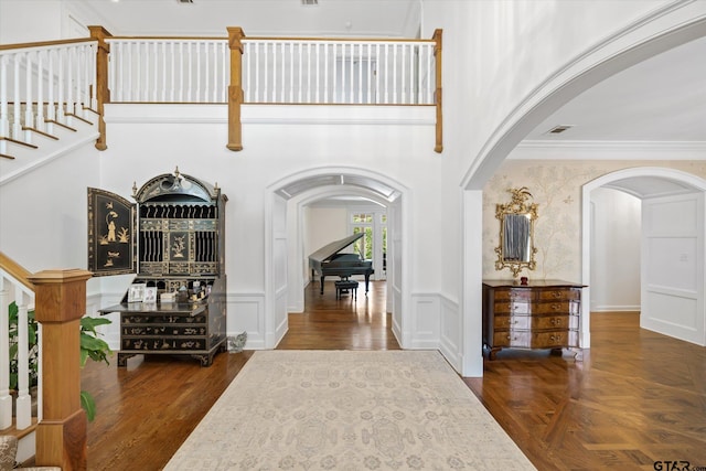 entrance foyer with a high ceiling, dark parquet flooring, and crown molding