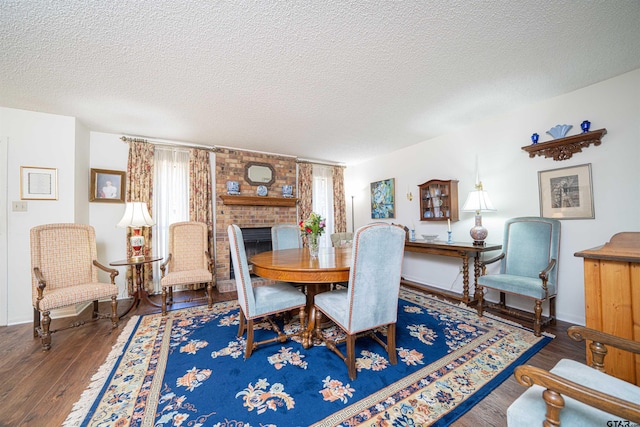 dining area featuring dark wood-type flooring, a textured ceiling, and a brick fireplace