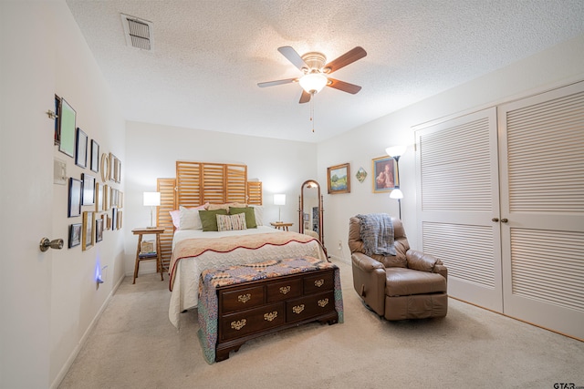 bedroom with a textured ceiling, light carpet, ceiling fan, and a closet