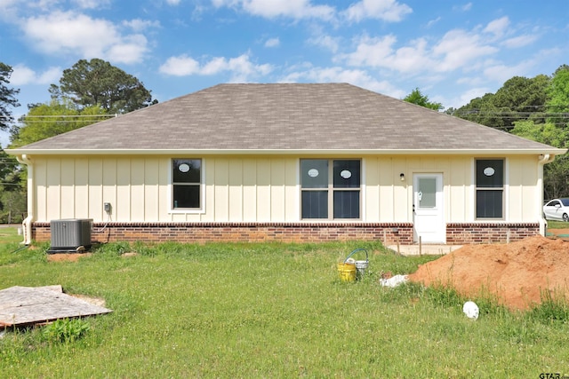 view of front of home with roof with shingles, central AC unit, brick siding, board and batten siding, and a front yard