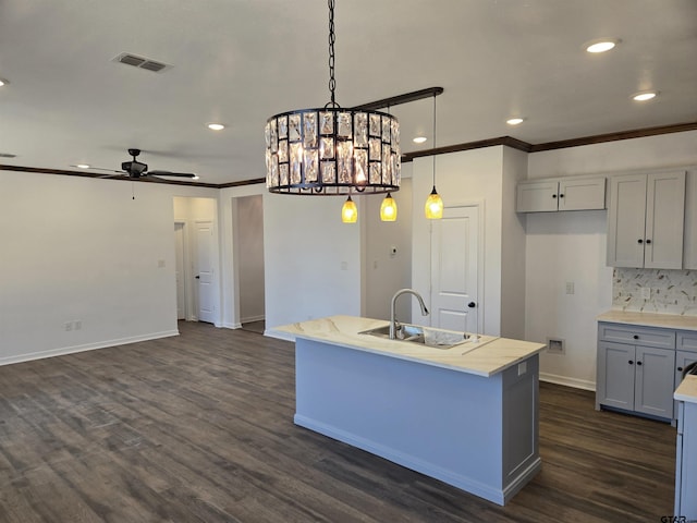 kitchen with pendant lighting, an island with sink, sink, crown molding, and dark wood-type flooring