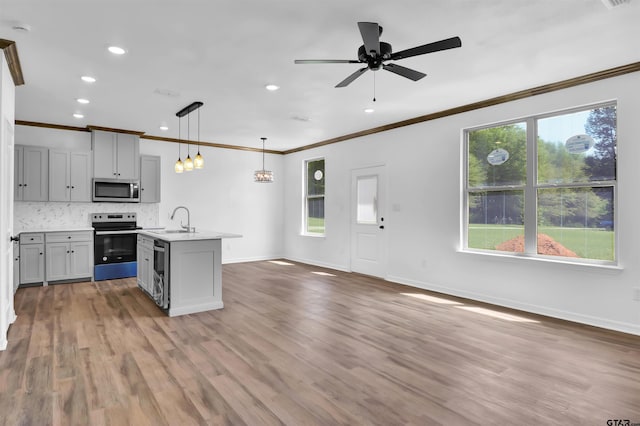 kitchen with ornamental molding, stainless steel appliances, light countertops, and a sink