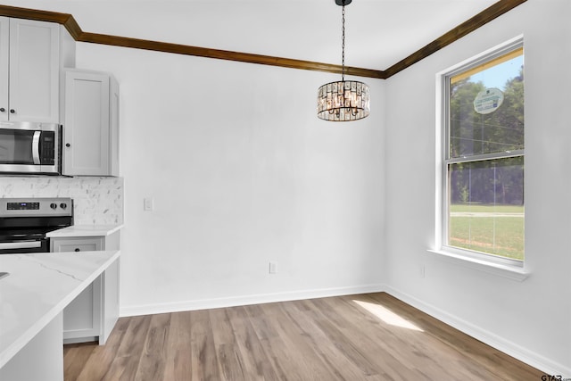 unfurnished dining area featuring light wood-type flooring, baseboards, a notable chandelier, and crown molding