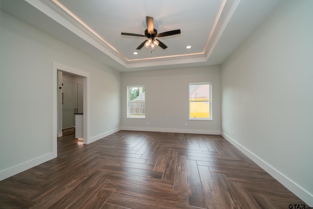 empty room featuring ceiling fan, a raised ceiling, and dark parquet floors