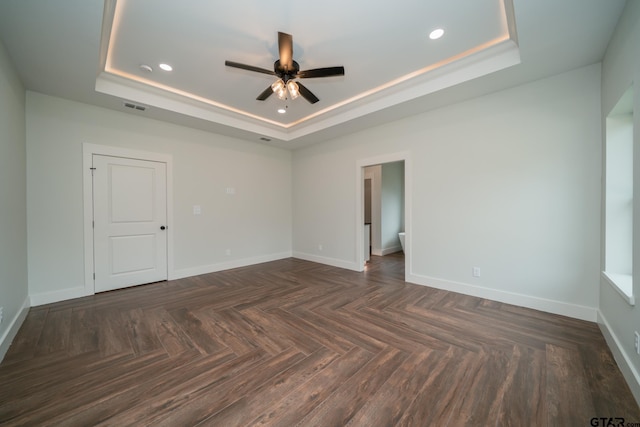 unfurnished room with dark parquet flooring, ceiling fan, and a raised ceiling