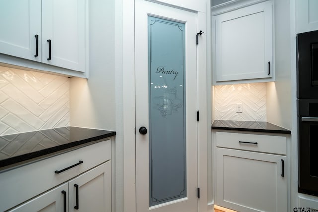 kitchen with dark stone countertops, tasteful backsplash, white cabinetry, and stainless steel oven