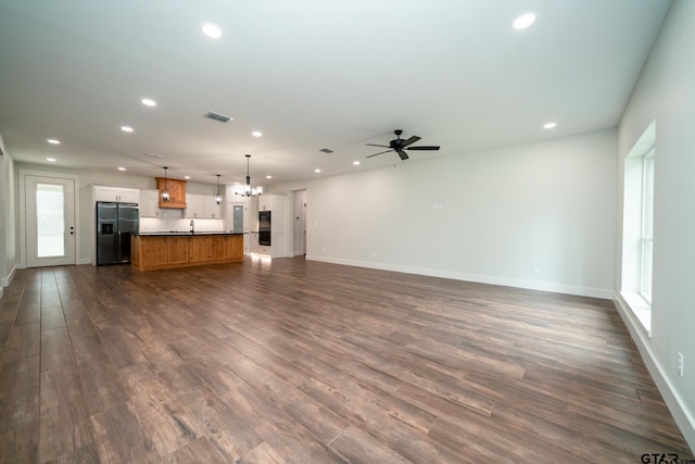 unfurnished living room featuring dark wood-type flooring, ceiling fan with notable chandelier, a healthy amount of sunlight, and sink