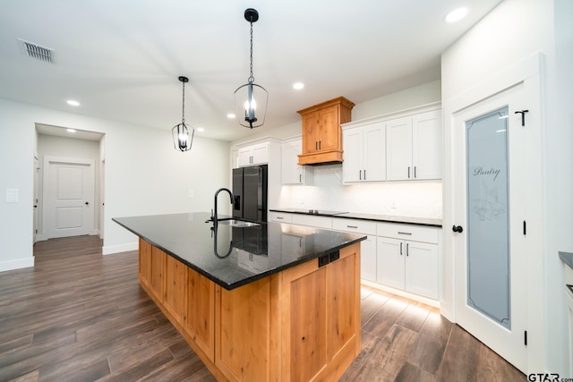 kitchen with dark hardwood / wood-style flooring, hanging light fixtures, sink, an island with sink, and white cabinetry