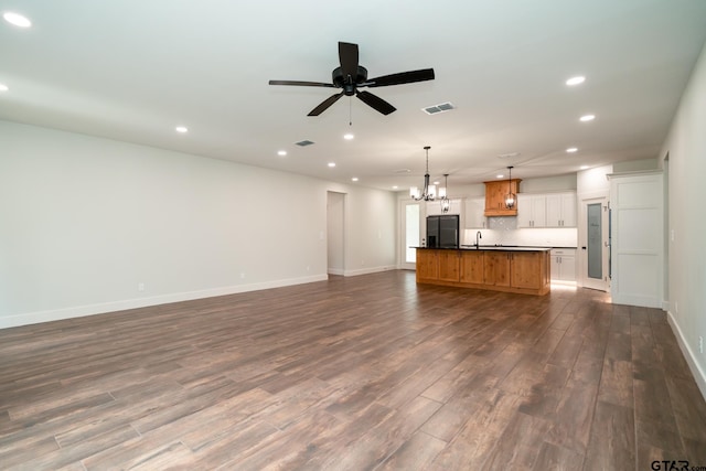 unfurnished living room featuring ceiling fan with notable chandelier, sink, and dark hardwood / wood-style flooring