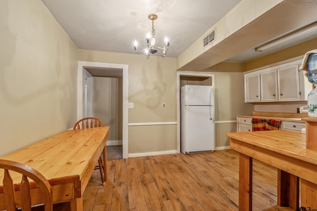 kitchen featuring pendant lighting, white cabinets, white refrigerator, an inviting chandelier, and light hardwood / wood-style flooring