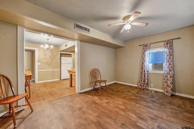 empty room with cooling unit, ceiling fan with notable chandelier, wood-type flooring, and a textured ceiling