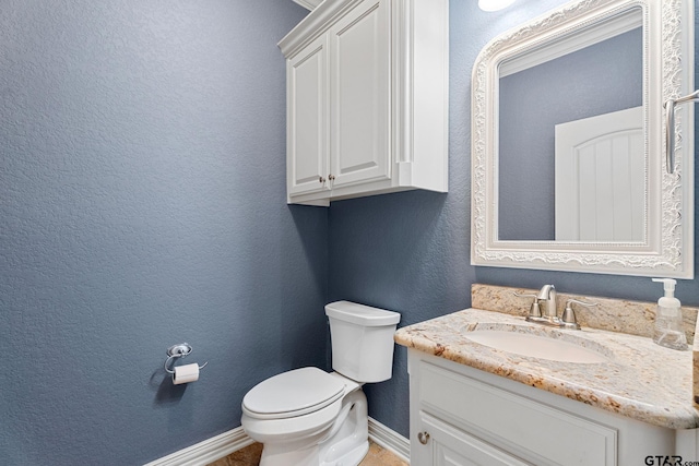 bathroom with toilet, vanity, baseboards, and a textured wall