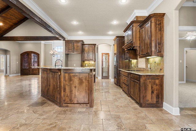 kitchen featuring stone tile floors, baseboards, arched walkways, a sink, and decorative backsplash