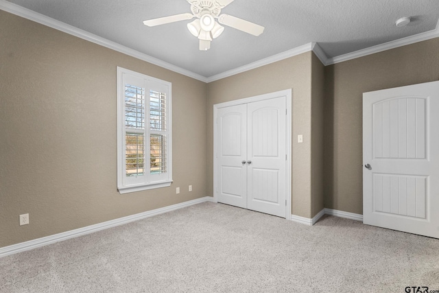 unfurnished bedroom with baseboards, a closet, a textured ceiling, crown molding, and carpet flooring