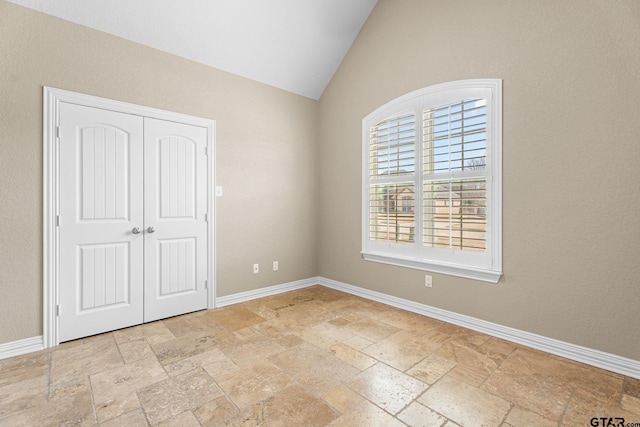 unfurnished bedroom with a closet, vaulted ceiling, baseboards, and stone tile flooring