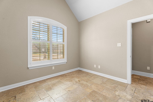 spare room featuring stone tile floors, baseboards, and vaulted ceiling