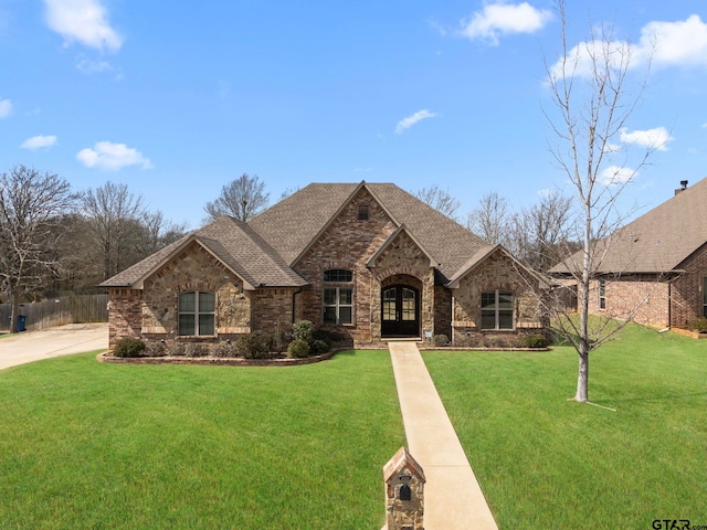 french country style house featuring stone siding, french doors, a front lawn, and roof with shingles