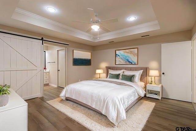 bedroom with ceiling fan, a raised ceiling, a barn door, dark hardwood / wood-style flooring, and ensuite bathroom