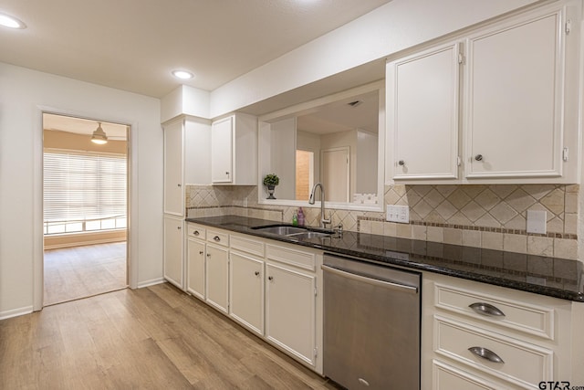 kitchen with dark stone counters, white cabinets, sink, stainless steel dishwasher, and light hardwood / wood-style floors