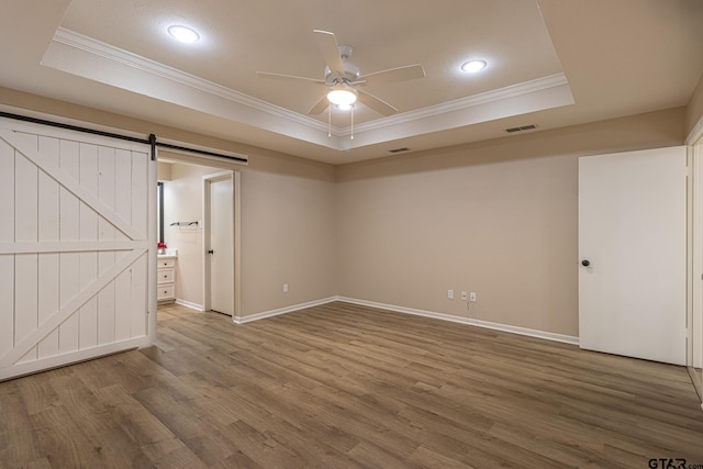 spare room with a tray ceiling, a barn door, crown molding, and wood-type flooring