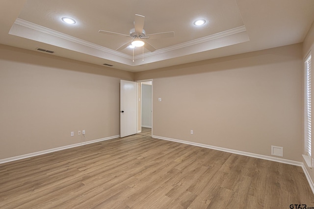 spare room featuring a raised ceiling, ceiling fan, ornamental molding, and light wood-type flooring