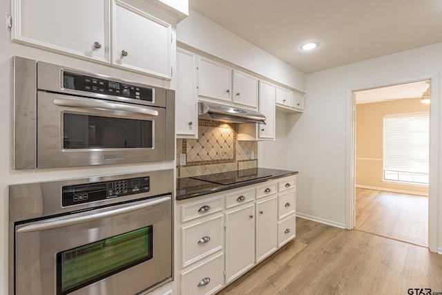 kitchen featuring dark stone counters, white cabinets, black electric stovetop, light hardwood / wood-style flooring, and tasteful backsplash