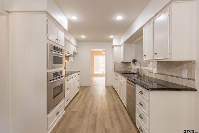 kitchen featuring dark stone counters, white cabinets, sink, light hardwood / wood-style flooring, and stainless steel appliances