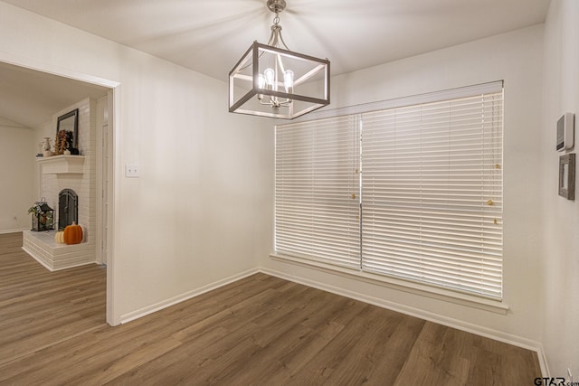 unfurnished dining area featuring a notable chandelier, dark hardwood / wood-style floors, and a brick fireplace