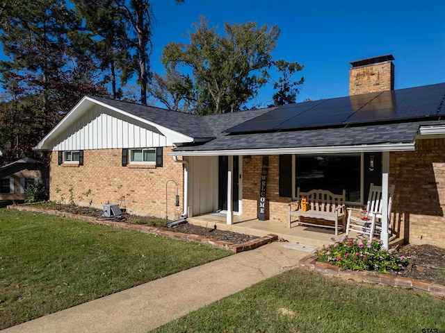 rear view of property featuring covered porch, solar panels, and a lawn